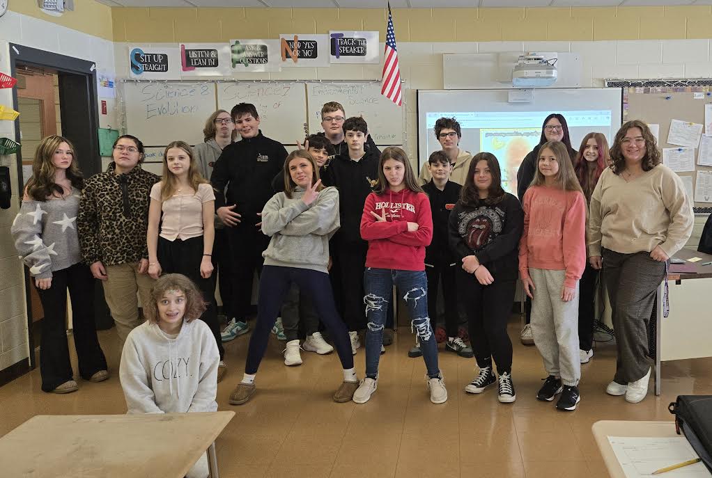 A group of students posing together, smiling at the camera. They are standing close, some with arms around each other, showing a sense of camaraderie and teamwork.