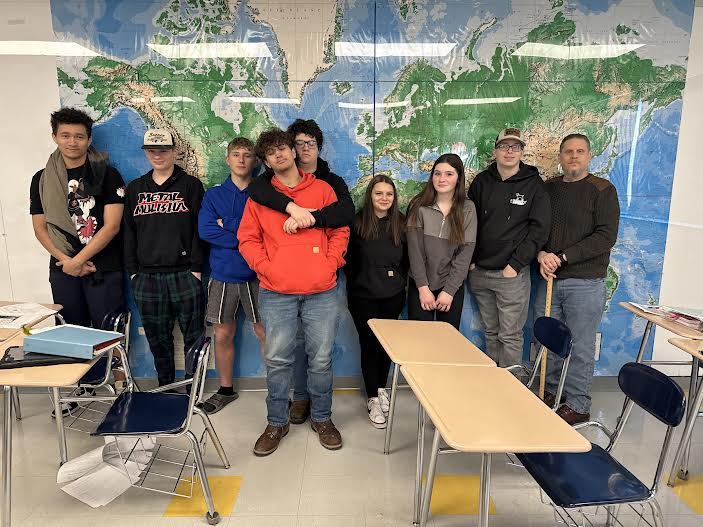 A group of students posing together, smiling at the camera. They are standing close, some with arms around each other, showing a sense of camaraderie and teamwork.