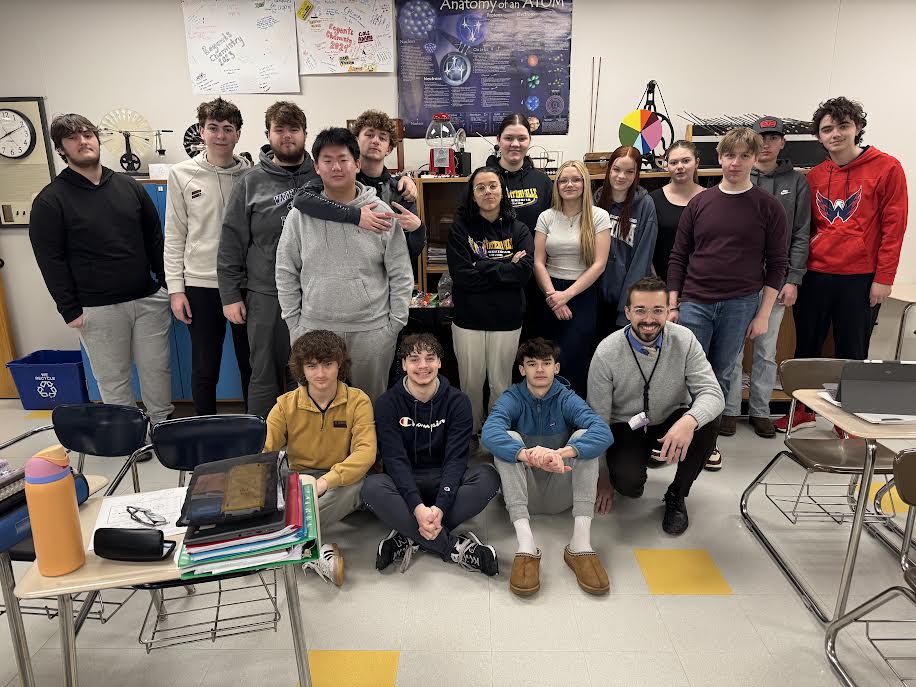 A group of students posing together, smiling at the camera. They are standing close, some with arms around each other, showing a sense of camaraderie and teamwork.