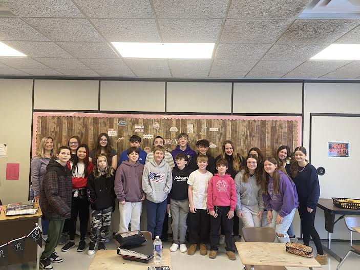 A group of students posing together, smiling at the camera. They are standing close, some with arms around each other, showing a sense of camaraderie and teamwork.