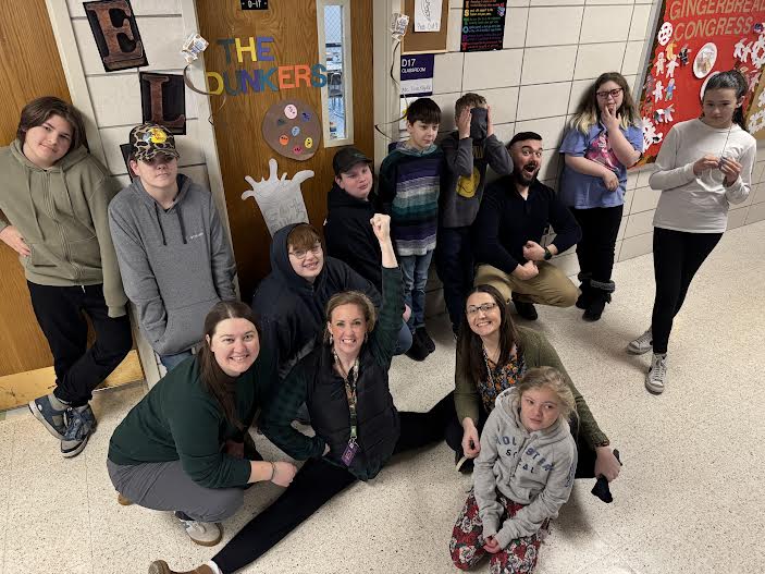 A group of students posing together, smiling at the camera. They are standing close, some with arms around each other, showing a sense of camaraderie and teamwork.