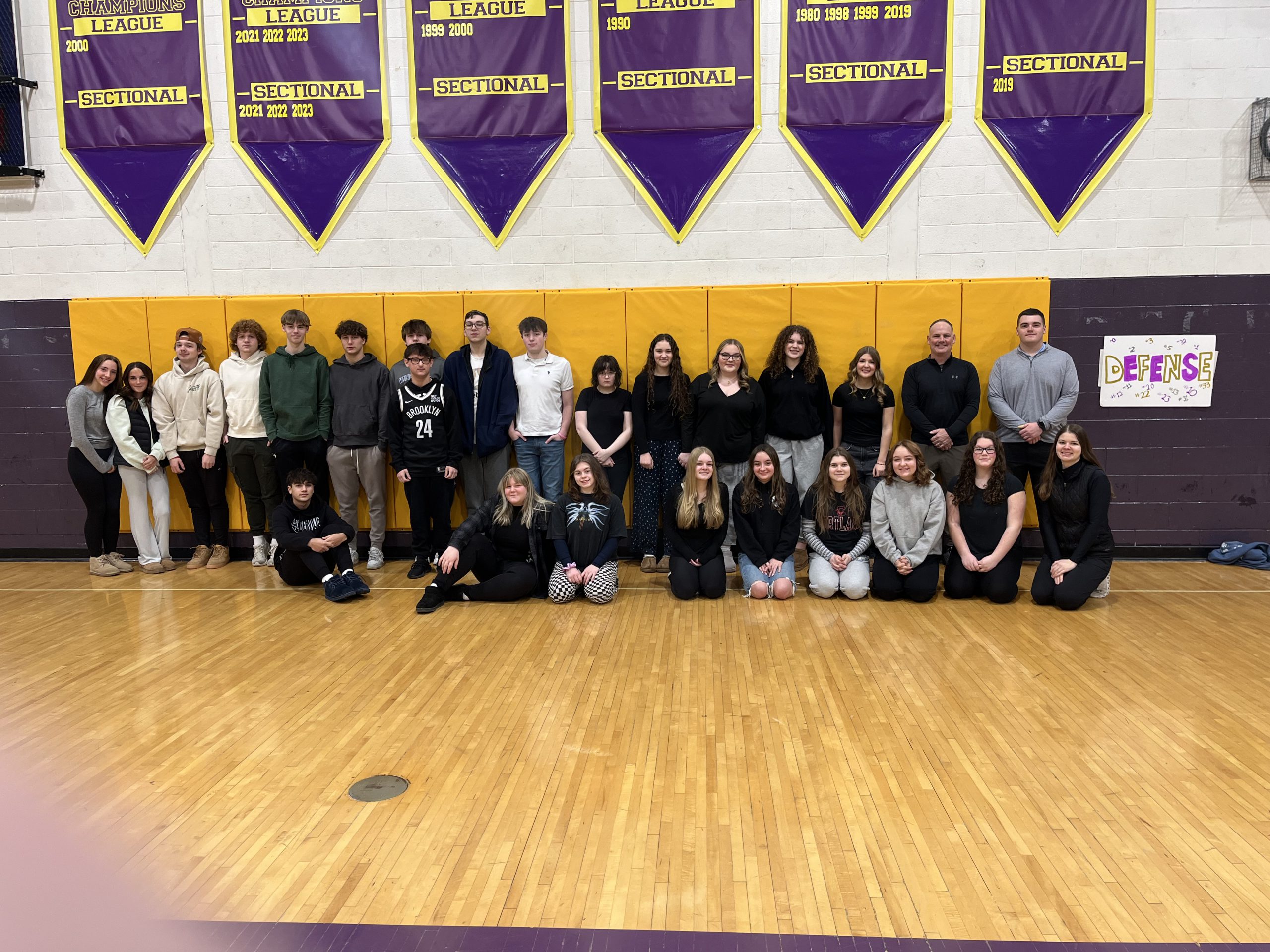 A group of students posing together, smiling at the camera. They are standing close, some with arms around each other, showing a sense of camaraderie and teamwork.