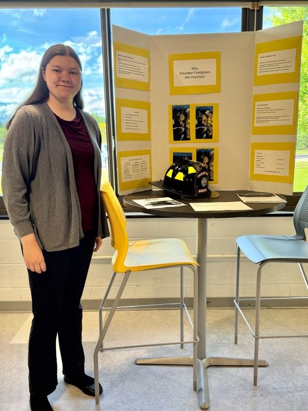 Photo of Abigail Dapson and poster with Why Volunteer Firefighters Are Important
