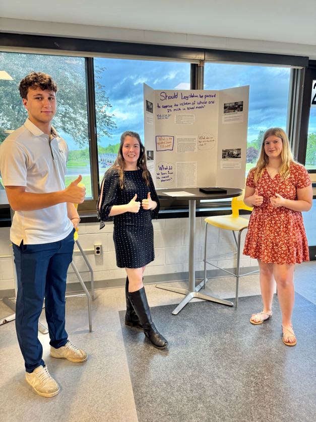 Photo of Allyson Ford, Olivia Ford, Quinnlan Mayne with poster of Should Whole & 2% Milk Be Included in School Meals?