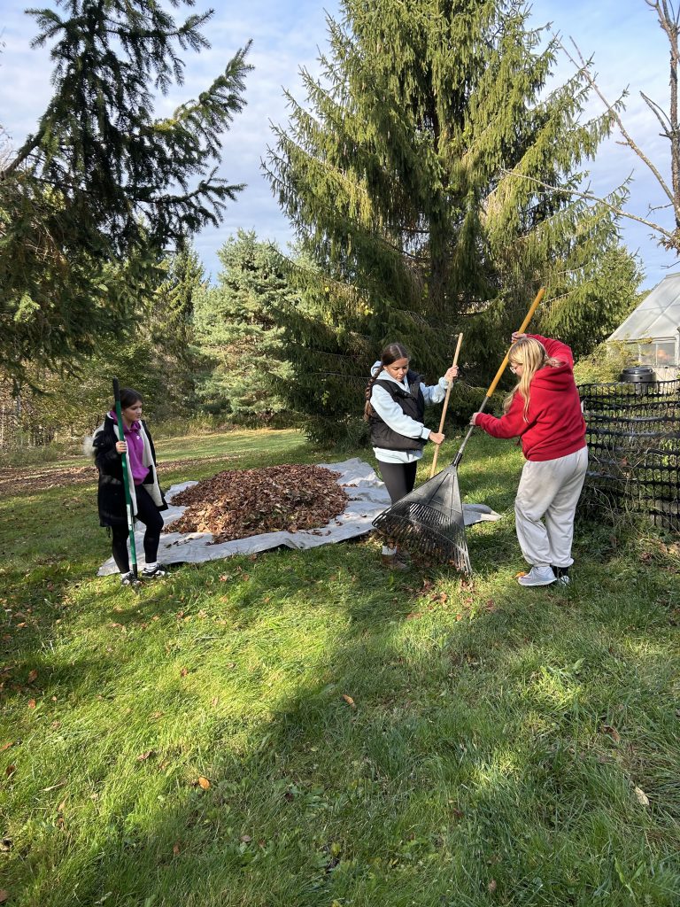 three students raking leaves onto a big brown tarp
