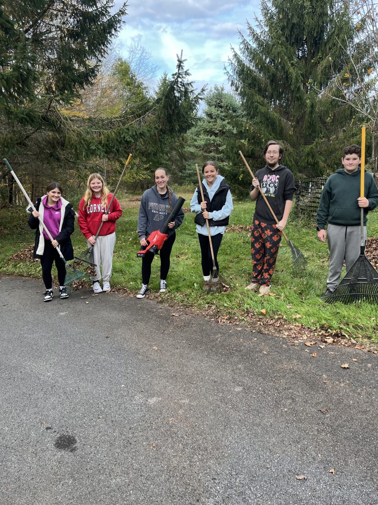 six students pose for a photo five students are holding rakes and one student has a leaf blower