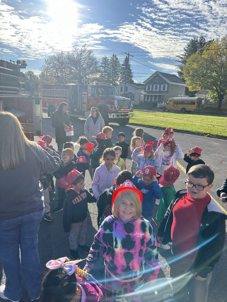 A group of students gathers around a firetruck as a volunteer firefighter explains its features and equipment.