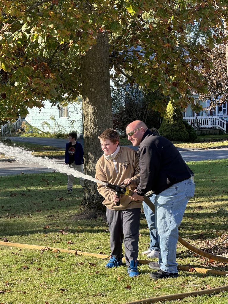 A firefighter assists a student in holding and aiming a fire hose during a safety demonstration.