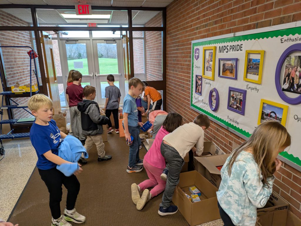 Twelve elementary school students sort donated food items and pack them into cardboard boxes during a school-organized food drive.