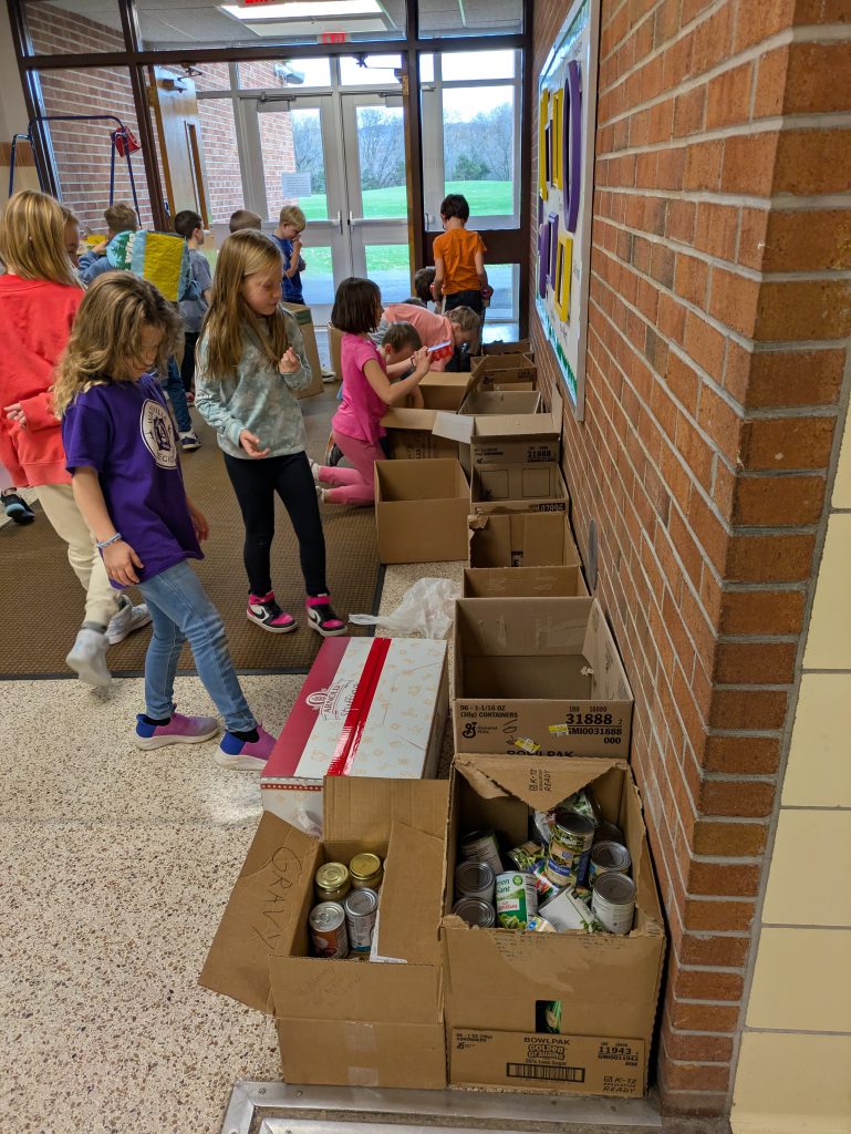 Twelve elementary school students sort donated food items and pack them into cardboard boxes during a school-organized food drive.