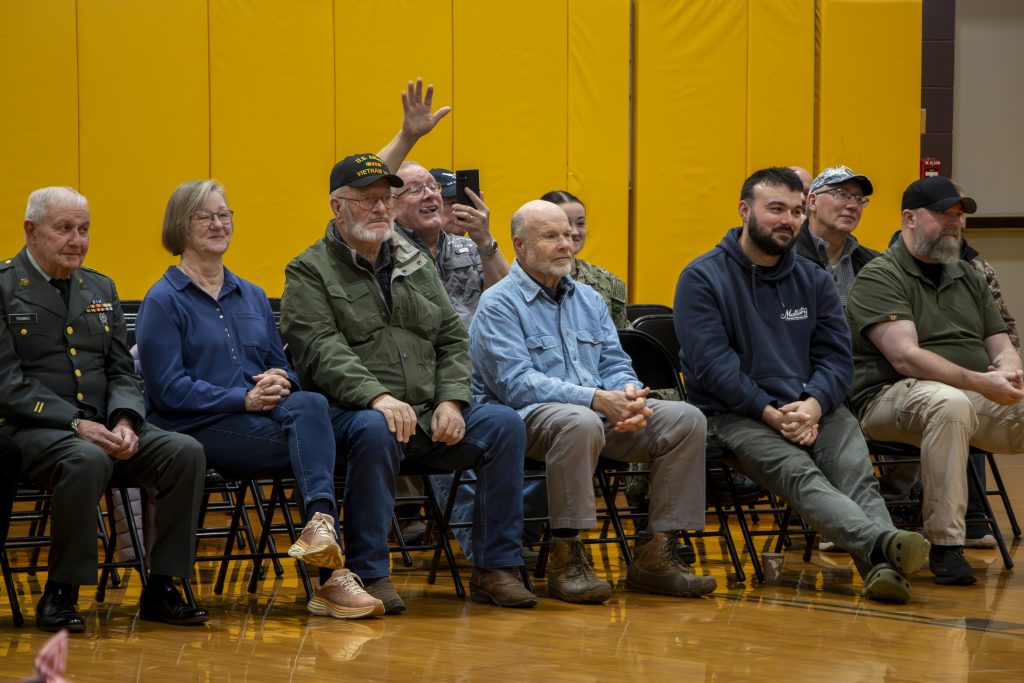 group of eight adults seated in front of a bright yellow background, with one person raising their hand.
