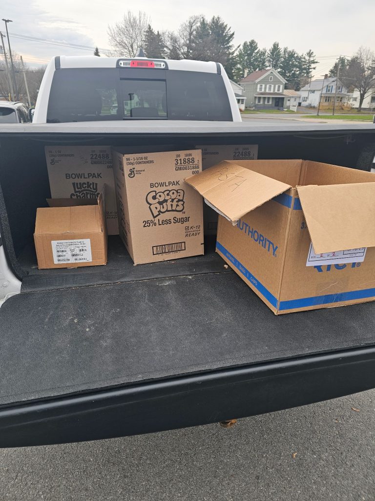 A gray pickup truck loaded with cardboard boxes filled with donated food items from a community food drive.