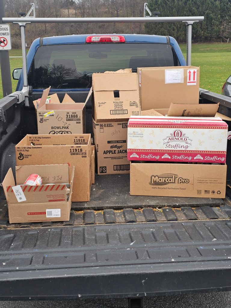 A blue pickup truck loaded with cardboard boxes filled with donated food items from a community food drive.