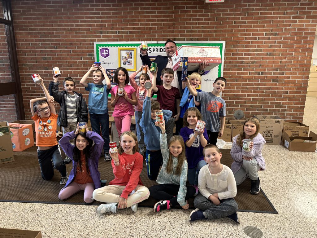 Mr. Perrone’s class poses for a group photo, each student proudly holding a canned food item to support the school’s food drive.