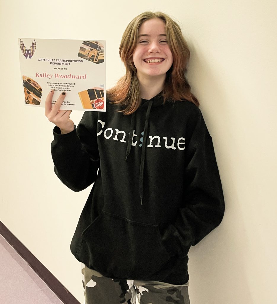 Eighth grade student smiling while holding a certificate, dressed in a black sweatshirt and camouflage army pants.