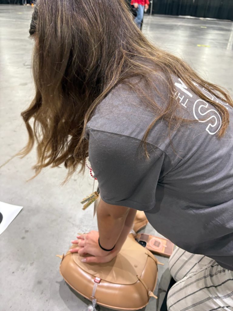The image shows a person wearing a gray shirt with a logo, bending down and examining something on the floor.